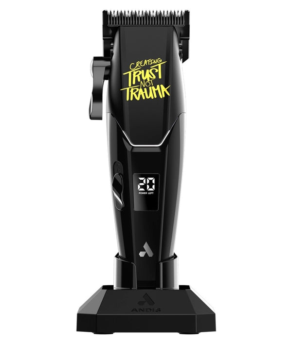 Black Andia cordless hair clippers with a yellow 'Creating Trust Not Trauma' graphic on the body, standing on a matching black charging dock against a white background.