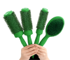 Four green hairbrushes held together by two hands against a solid white background. Three are round barrel brushes and one is an oval paddle brush, all with dense green bristles.