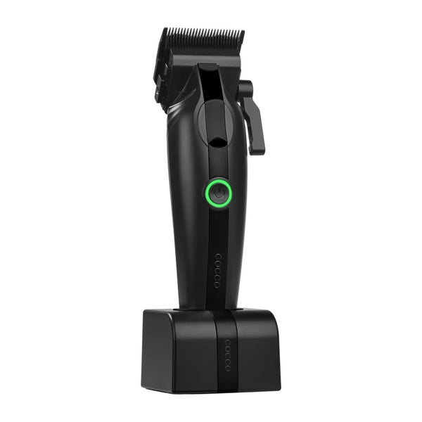 A black cordless hair clipper with a green power button, shown standing upright on its charging dock against a solid white background.